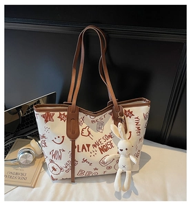 Detail of graffiti tote bag with rabbit charm, laptop, and books on a stylish workspace