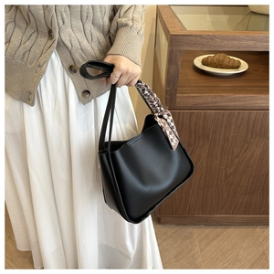 Detail of black leather tote bag with elegant brown checkered scarf tied on the handle