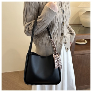 Detail of black faux leather tote bag with checkered scarf on handle for casual style