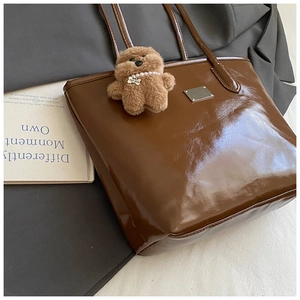 Détail du cabas marron brillant avec breloque ours sur fond de magazine chic