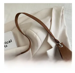 Detail of dark brown velvet tote bag handle with silver metal rings on white blazer