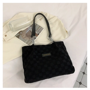 Detail of black checkered corduroy tote bag featuring silver chain and branded label