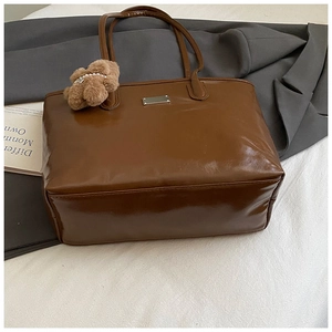 Détail d'un sac cabas en cuir marron foncé avec logo métallique et pendentif ourson