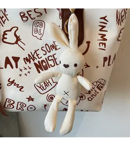 Close-up of a white fabric rabbit charm with gold metal clasp on a stylish tote bag