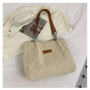Detail of checkered woven tote bag showing leather strap and fashion label on creamy fabric