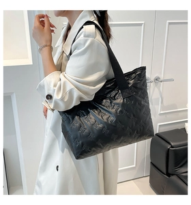 Detail of black padded tote bag with embossed bow patterns and wide fabric shoulder strap