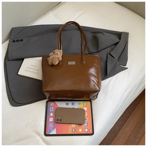 Détail d'un grand sac cabas marron avec un ourson en peluche et plaque en métal chic