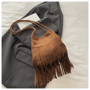 Gros plan du sac bandoulière en daim marron avec franges sur fond de costume gris