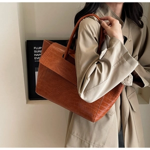 Dettaglio borsa shopper marrone con stampa coccodrillo e trench coat kaki