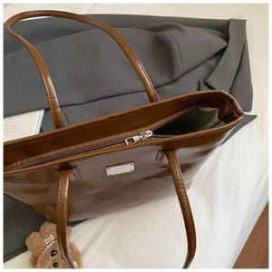 Détail du sac cabas en cuir marron montrant la fermeture éclair et la plaque en métal
