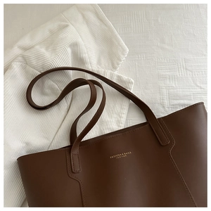 Detail of dark brown leather tote bag showing fine stitching and gold logo text
