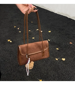 Detail of dark coffee suede shoulder bag with cute plush bear charm on autumn leaves