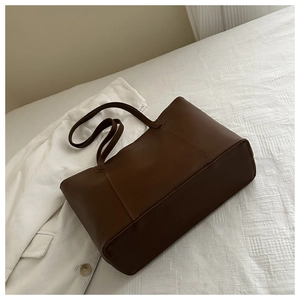 Detail of dark brown leather tote bag showing fine stitching on a white textured backdrop