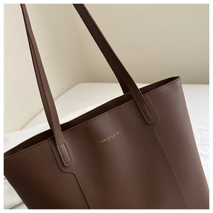 Close-up of matte dark brown leather tote bag showing fine stitching and gold lettering