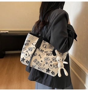 Detail of white tote bag featuring black graffiti prints and a plush bunny charm