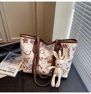 Close-up of white graffiti tote bag with brown leather handles and plush bunny charm