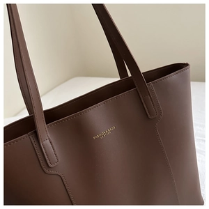Macro detail of dark brown leather tote bag with gold lettering and stitched seams