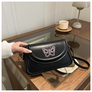 Détail d'un sac bandoulière noir avec broderie papillon rose sur une table en bois