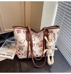 Detail of a white graffiti tote bag with brown trim and a cute bunny plush charm
