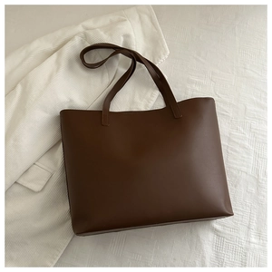Overhead view of a dark brown matte leather tote bag with long straps on a white fabric
