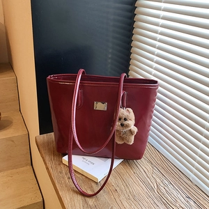 Sac cabas minimaliste en cuir verni bordeaux avec breloque ours sur un rebord de fenêtre
