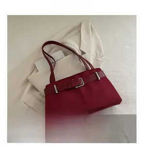 Detail of wine red suede shoulder bag with metallic buckle against a beige blazer