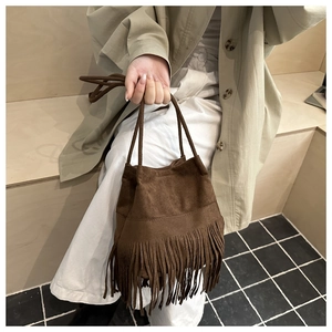 Détail d'un sac seau en daim marron avec de longues franges et double poignée fine