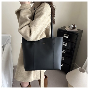 Detail of a large black faux leather tote bag showing golden text on a beige wool coat