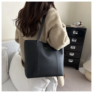 Fashionable black matte leather tote bag worn by a model in a minimalist home setting