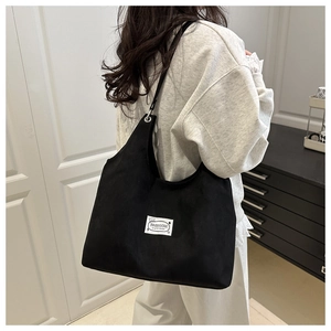Dettaglio della grande borsa tote in velluto nero con etichetta moda indossata da modella