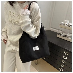 Detailed close-up of a black canvas tote bag with fashion label and silver metal eyelets