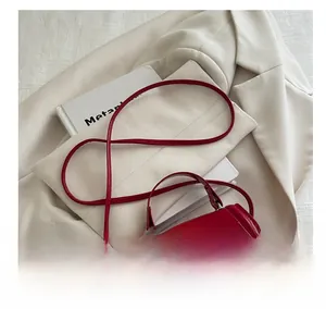 Detail of red patent leather square handbag with top handle on white blazer background