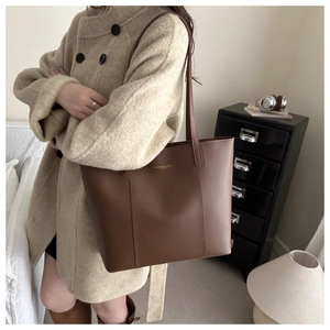 Close-up of brown leather tote bag with gold lettering shown on a model in wool coat