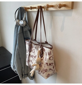 Detail of a large cream tote bag with brown trim and cute graffiti patterns on a hook
