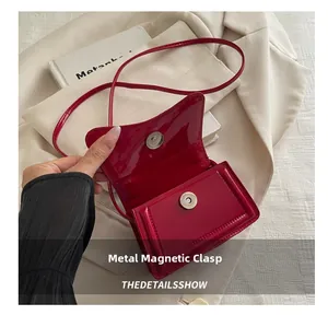Detail of glossy red patent leather crossbody bag with magnetic metal snap closure