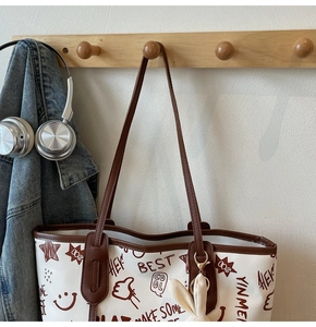 Detail of white graffiti tote bag with brown leather handles on a wooden wall hook