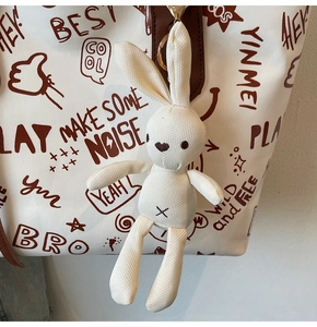 Close-up of a cute plush rabbit pendant with metal clasp on a canvas tote bag