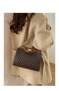 Detail of the vintage plaid flap bag with metallic clasp and leather handle on a coat