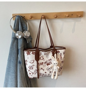 Detail of white tote bag with brown graffiti patterns and plush rabbit charm