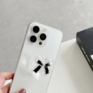 Close-up of a clear heart phone grip with a black bow detail on a white smartphone