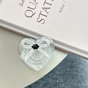 Close-up of heart-shaped transparent phone grip with silver bow and clover detail