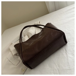 Detailed side view of dark brown faux crocodile leather tote bag on white fabric