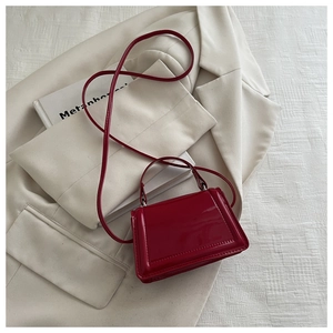 Detailed view of deep red patent leather mini crossbody bag on a beige blazer background