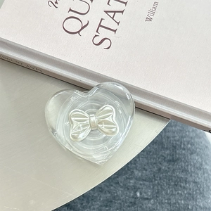 Macro view of transparent heart phone grip with a pearly white bow detail on a desk