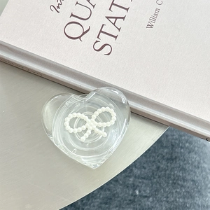 Detailed view of heart-shaped transparent phone grip with pearl bow on a minimalist desk
