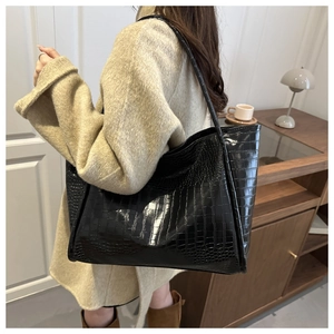 Close-up of black crocodile embossed tote bag texture worn by model in cozy interior