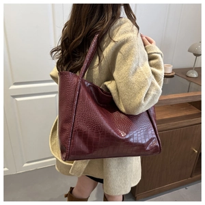 Detail of burgundy crocodile-embossed tote bag worn over shoulder for a classy look
