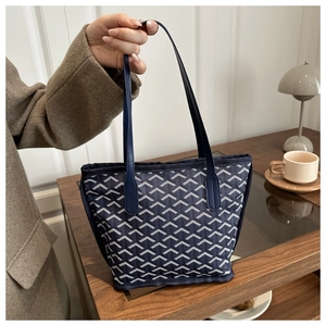 Detailed view of large tote bag with Y-pattern print and navy leather handles in cafe setting