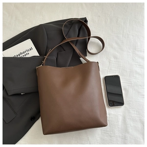 Flat lay of a large brown leather tote bag with office essentials on a white background