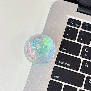 Macro shot of circular aurora glitter phone grip with green shimmer on a laptop keyboard
